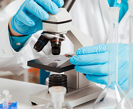 Profissional com luvas azuis realizando análise em microscópio no laboratório
